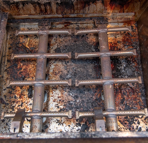 Two trellis shaped tubular metal pieces. Baked on grease and food is in the background.