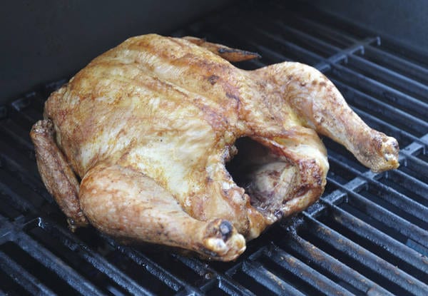A crispy brown whole chicken cooking on a gas grill.