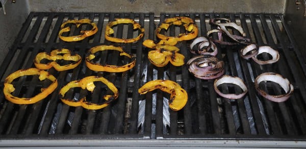 Peppers and onions cooking on a gas grill with pronounced brown sear marks.