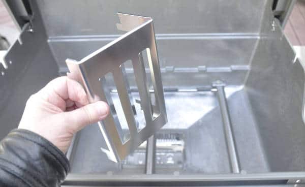 A left hand holding a shiny steel rectangular object with slots cut across it.