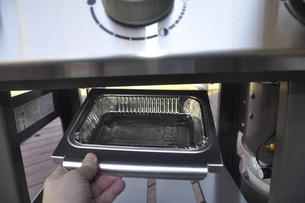 A left hand holding a small steel tray with a disposable aluminum foil liner inside.