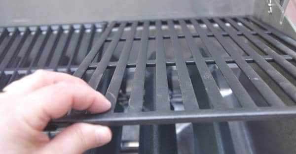 A left hand holds a black metal grid or grates. The surface of this grate is flat.