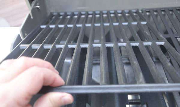 A left hand holds a black metal grid or grates. The surface of this grate is a row of upside down V-shaped metal bars.