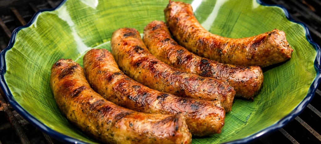 Five grilled chicken sausages in a green bowl.