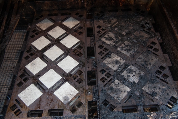Two metal. rectngular plates with grids of white, diamond-shaped objects. The plate on the right is blackened and charred