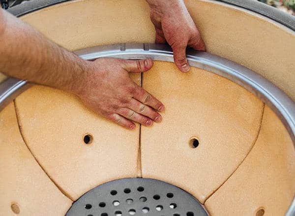 Two hands reach into the bottom of a round ceramic bowl. The bottom is made of several curved segments.