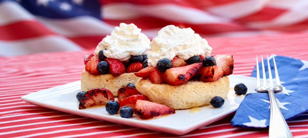 Grilled strawberry shortcake with whipped cream and blueberries on a white plate and a flag background