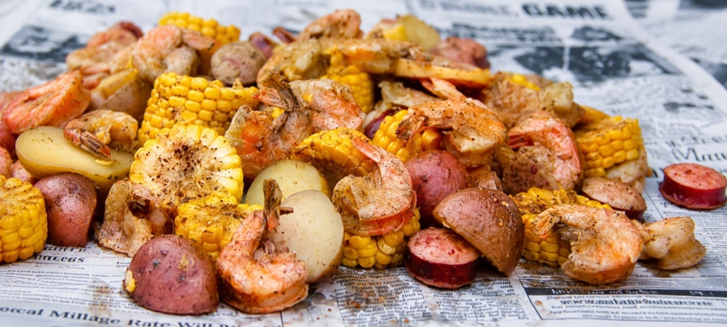Shrimp boil with potatoes and corn on newspaper.