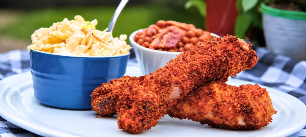 Two deep fried ribs on a plate along with noodle salad and baked beans