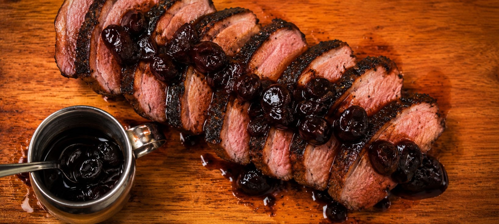Sliced duck breast topped with balsamic-cherry reduction and a glass container with more sauce on the side.