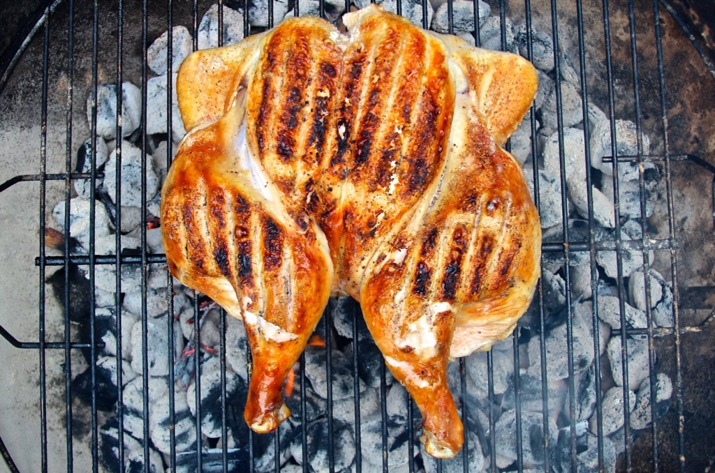 Spatchcocked chicken on the grill over burning charcoal