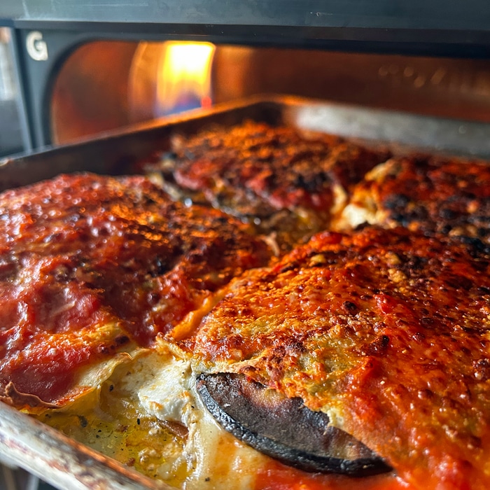 Pan of lasagna entering the pizza oven