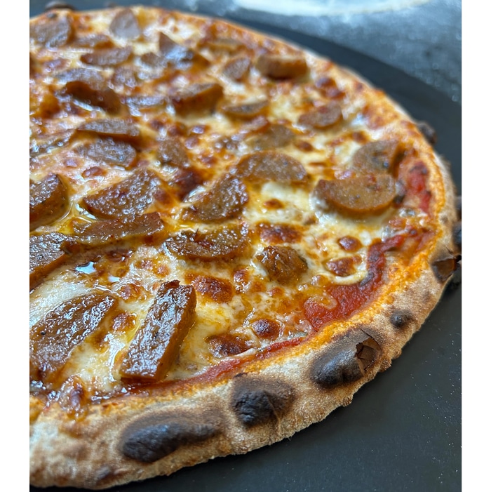 Finished sausage pizza coming out of the pizza oven