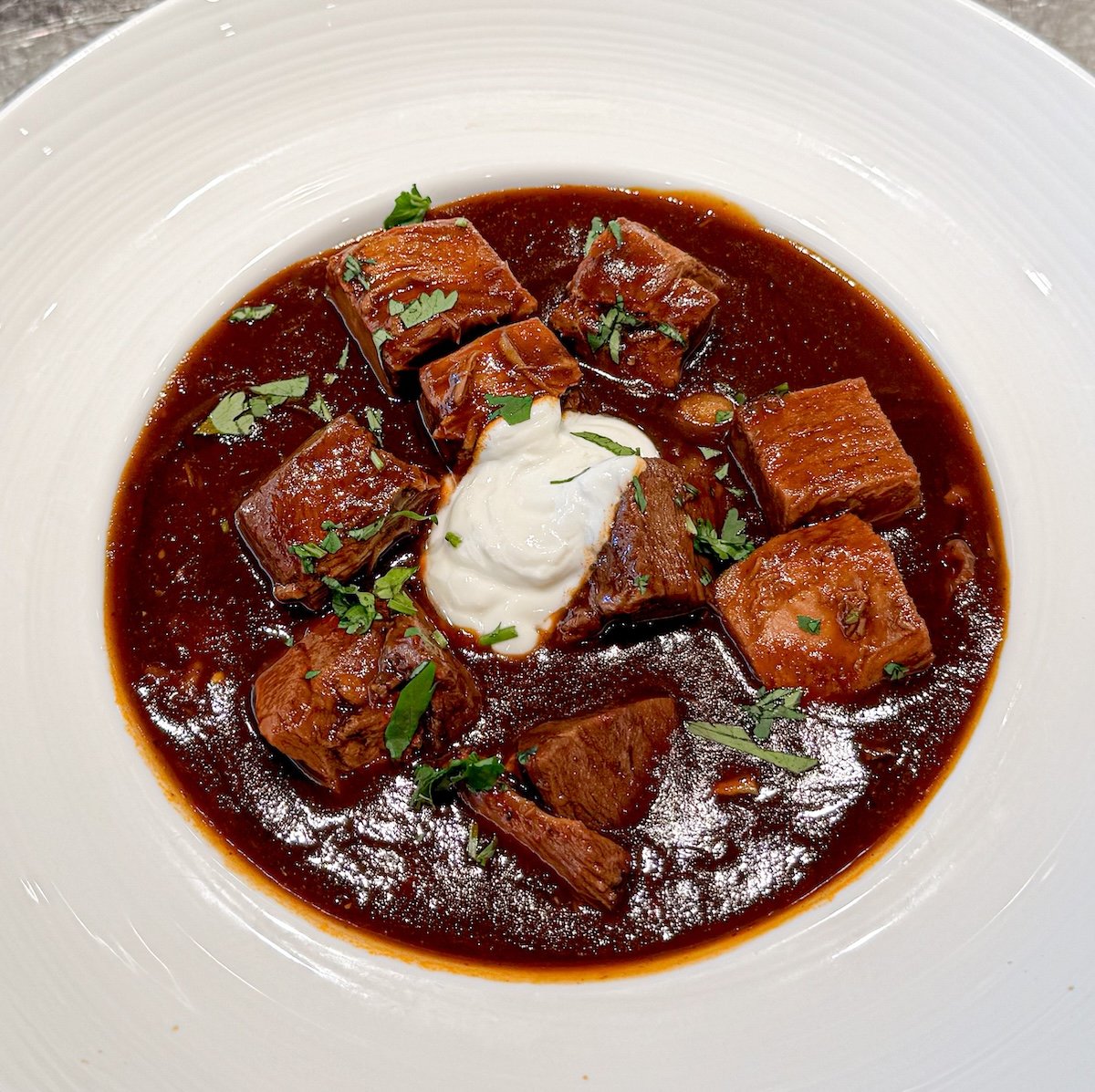 pozole rojo in a white bowl garnished with sour cream and cilantro.