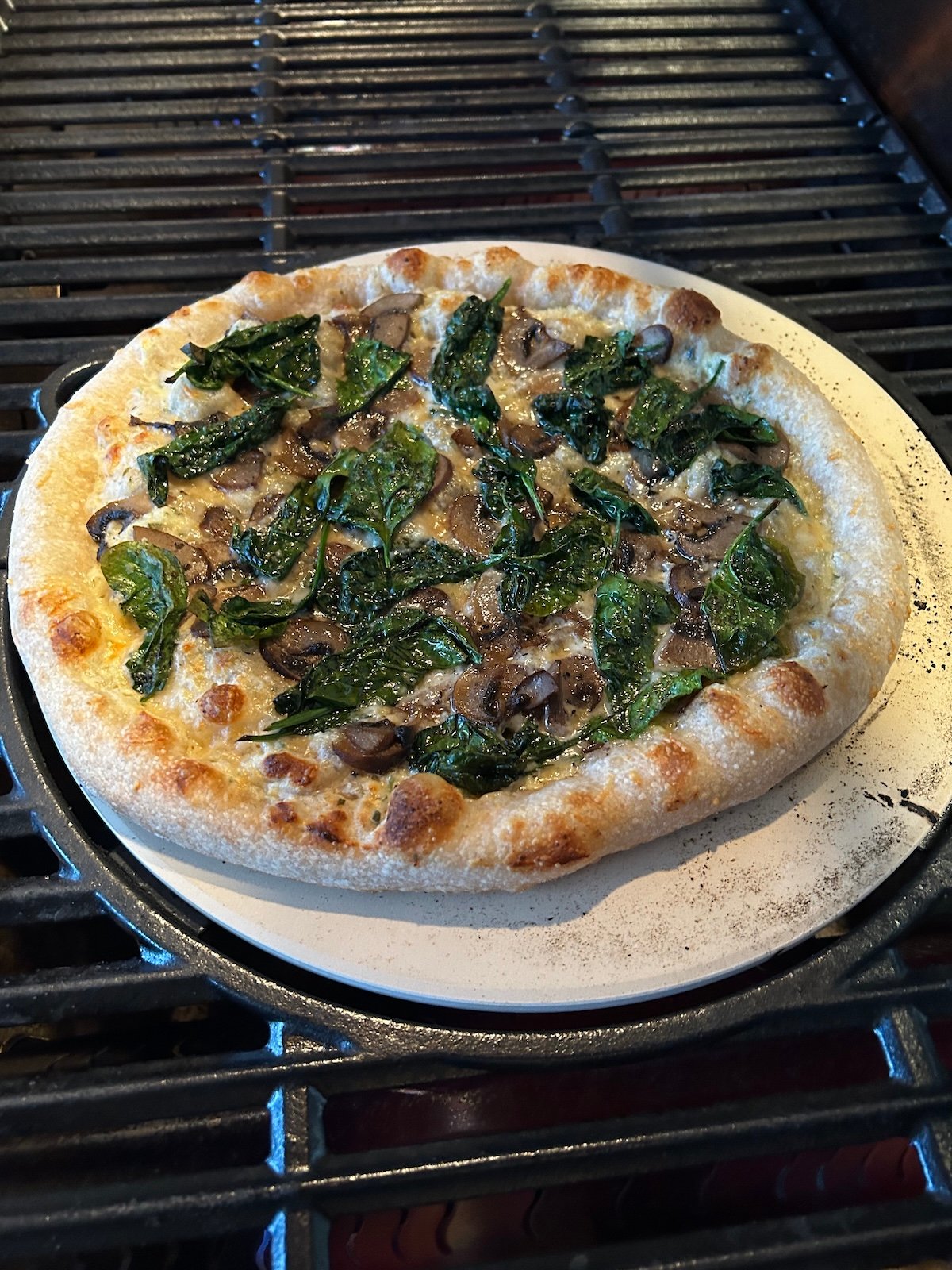 spinach and mushroom pizza on pizza stone on grill