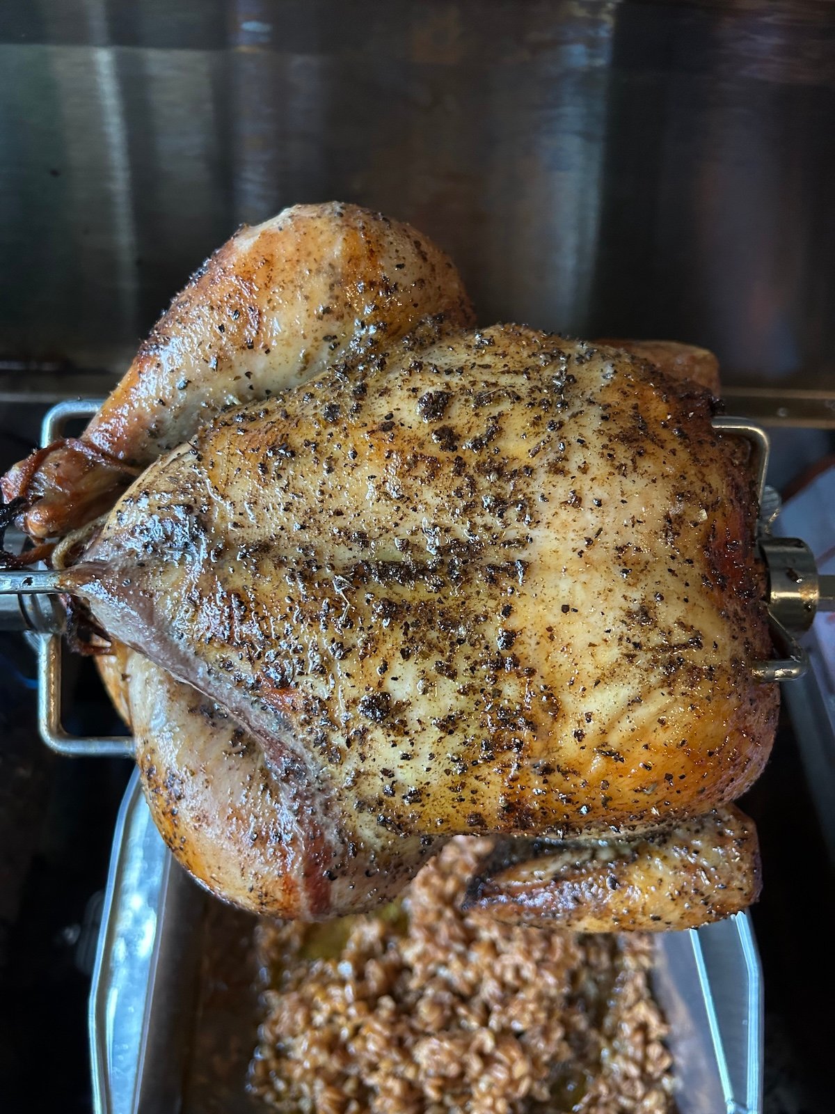 rotisserie chicken on grill with pan beneath