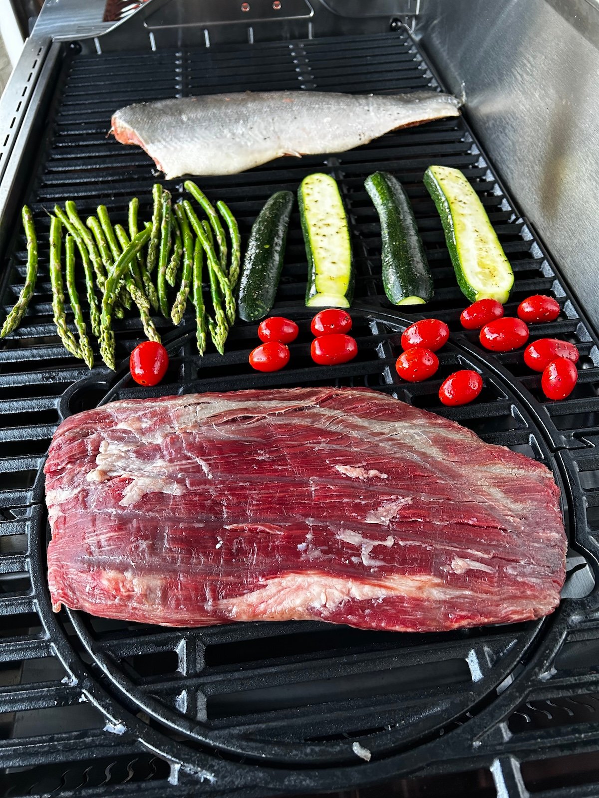 flank steak, salmon, asparagus, zucchini and cherry tomatoes on grill.