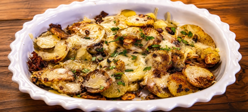 Cheese covered potatoes in a whit baking dish on a wooden surface