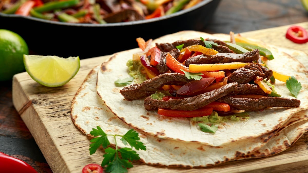 steak fajitas assembled on tortillas on a wooden board