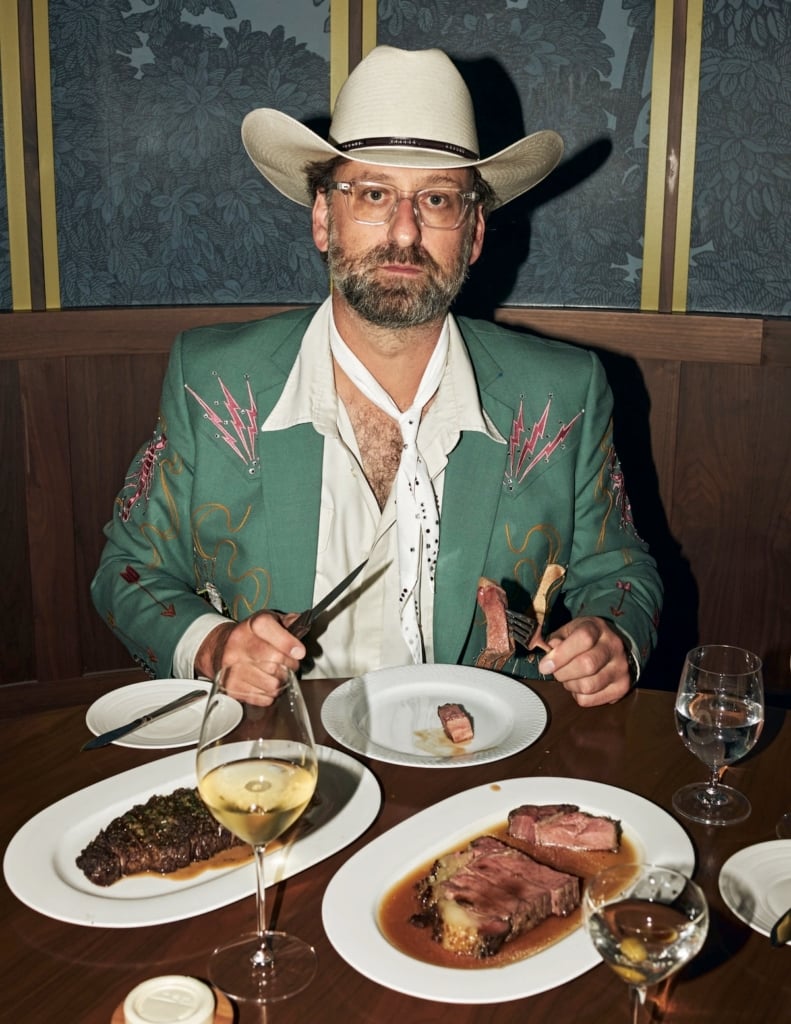 Eric Wareheim sitting down to a steak house meal wearing a cowboy hat.