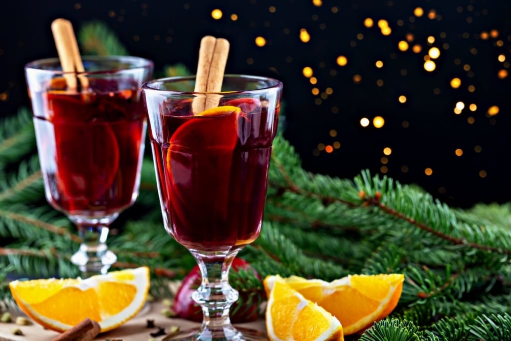 Swedish glogg mulled red wine in glass cups with cinnamon sticks and oranges with a Christmas background.