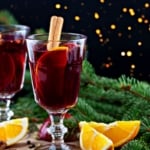 Swedish glogg mulled red wine in glass cups with cinnamon sticks and oranges with a Christmas background.