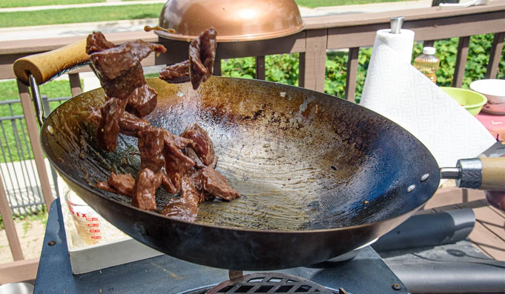 flipping meat in a wok outside on a charcoal chimney in a grill.