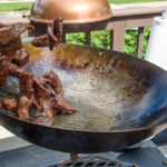 flipping meat in a wok outside on a charcoal chimney in a grill.