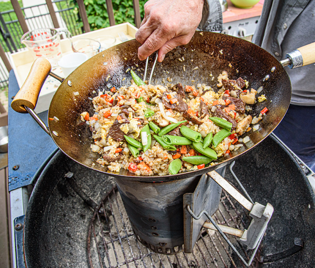 a person making stir fry outside in a wok on a charcoal chimney.