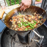 a person making stir fry outside in a wok on a charcoal chimney.