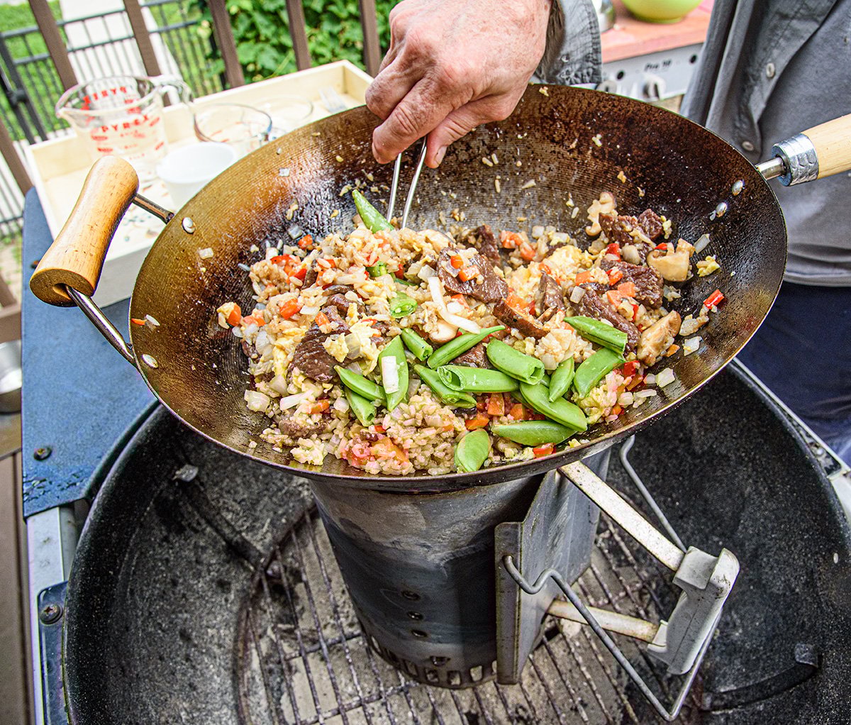a person making stir fry outside in a wok on a charcoal chimney.