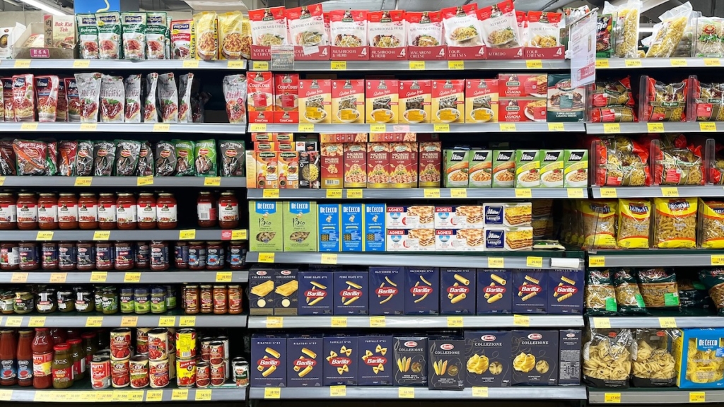 Processed food including dried pasta and canned tomatoes on a grocery store shelf