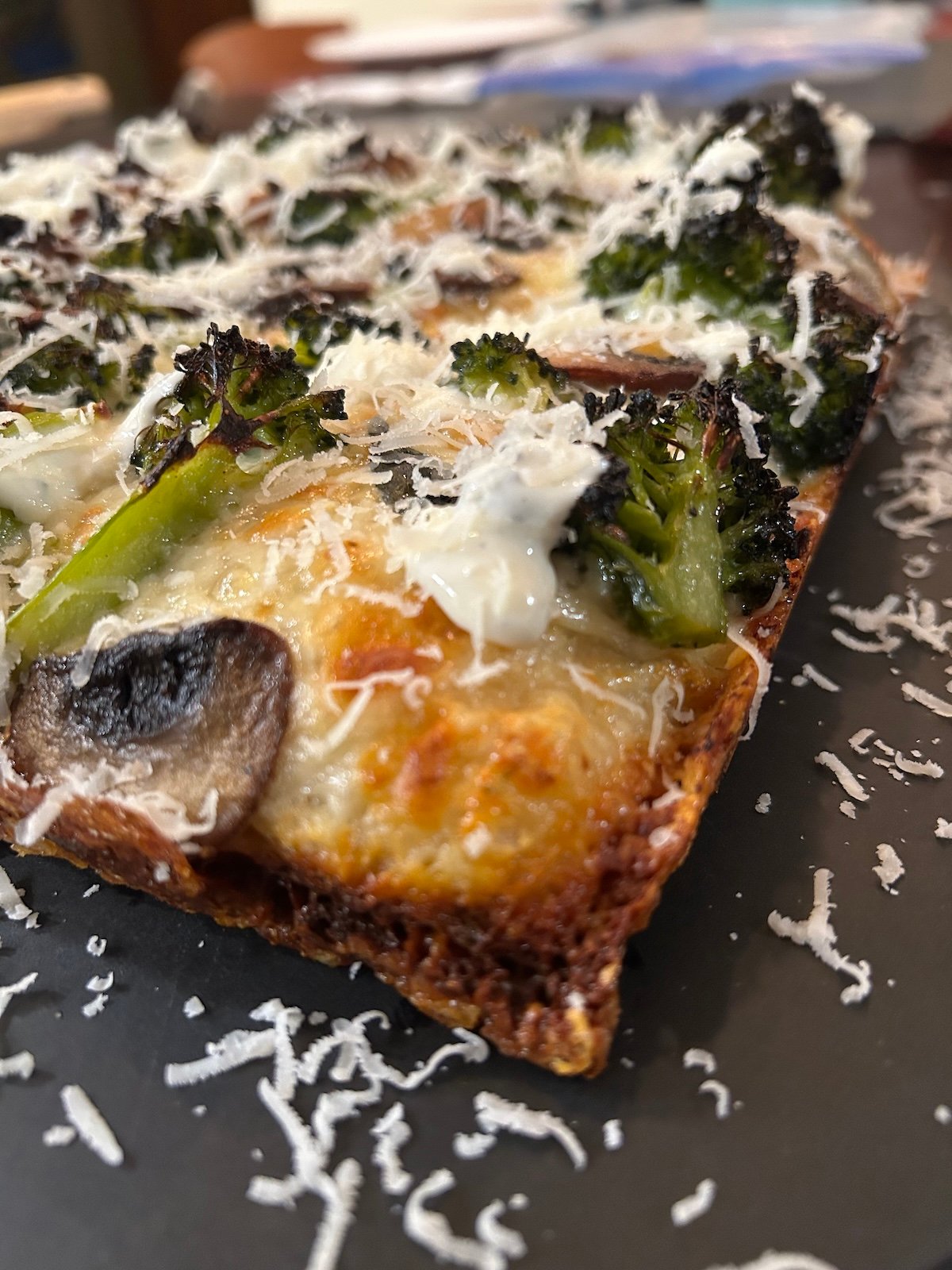 A baked Detroit style square pizza topped with broccoli, mushrooms, white sauce, and shredded Parmesan cheese, shown from the corner.