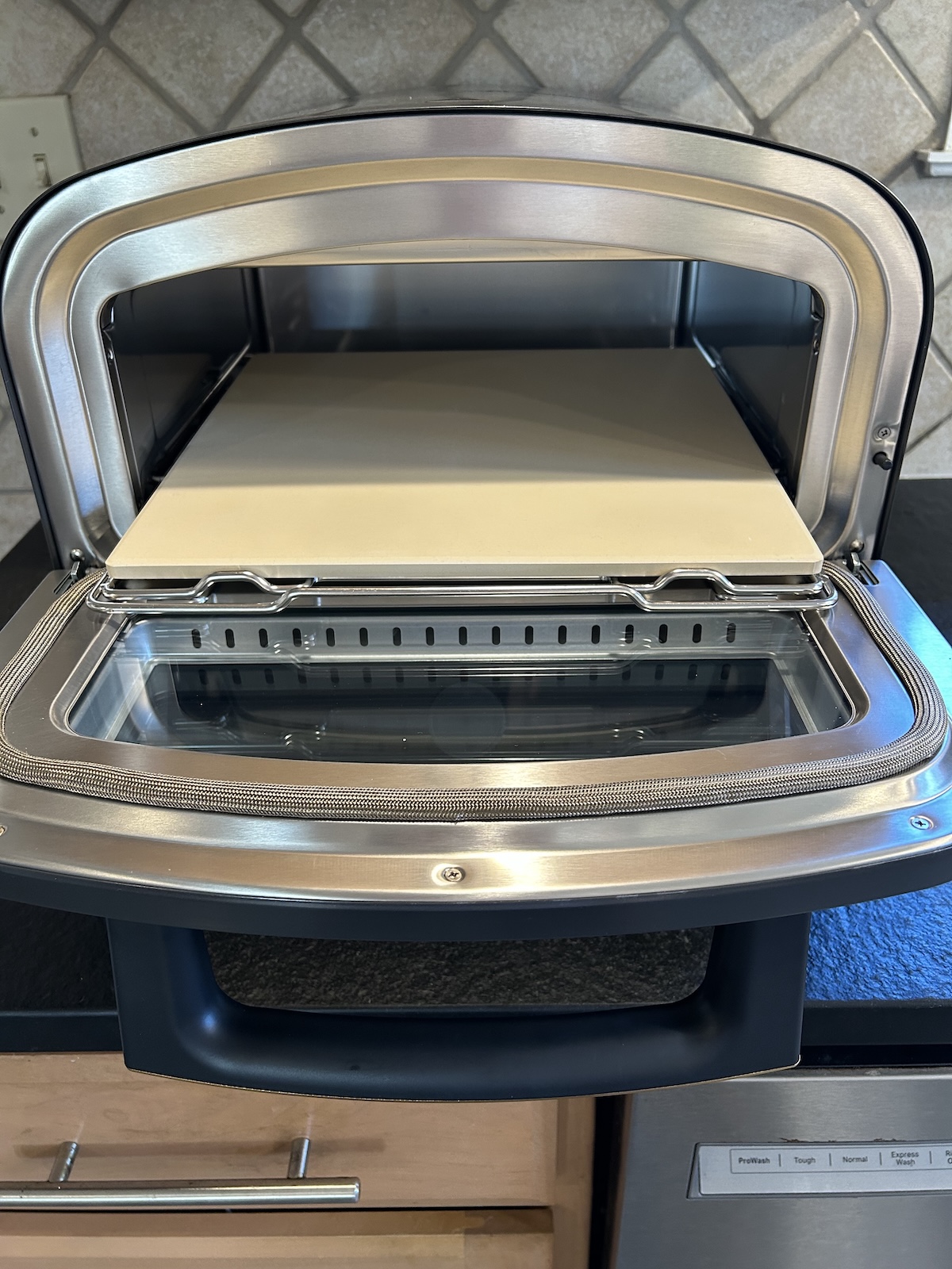 Current Model P smart pizza oven shown with the front door open and square pizza stone partially out of the oven on its slide-out rack.