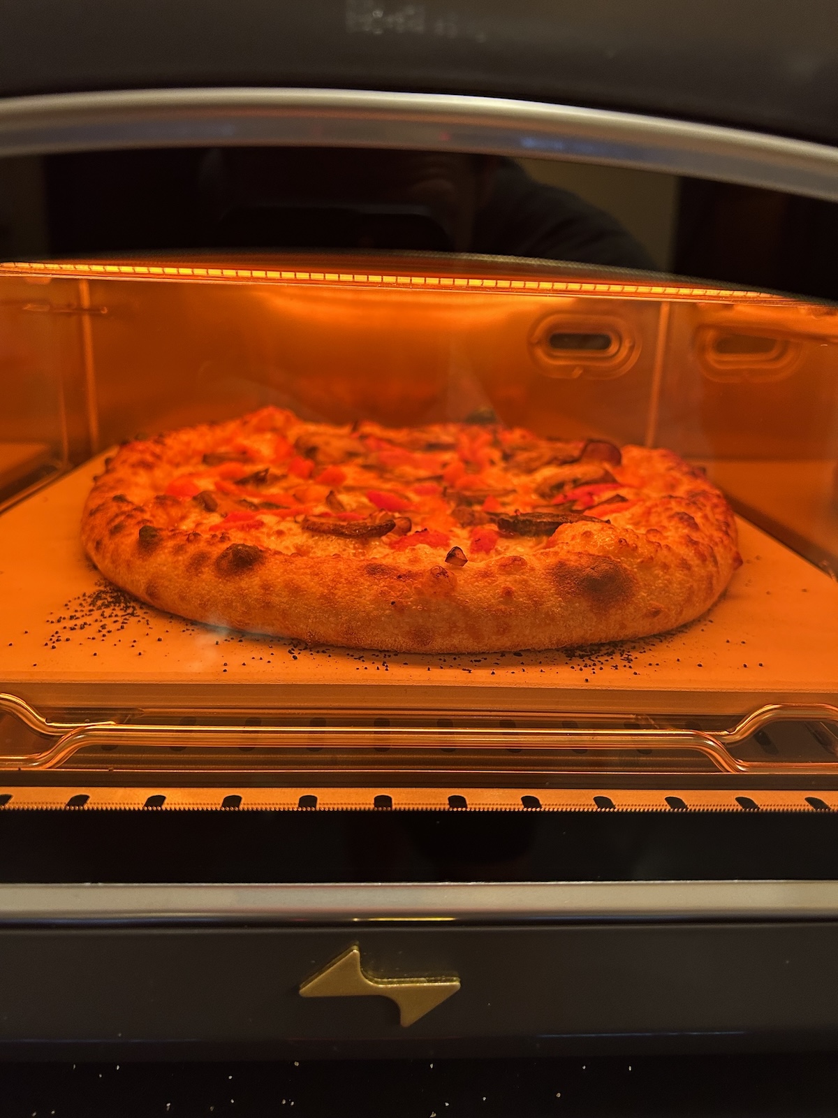 Pizza baking inside the Current Model P smart pizza oven shown through the glass front door.