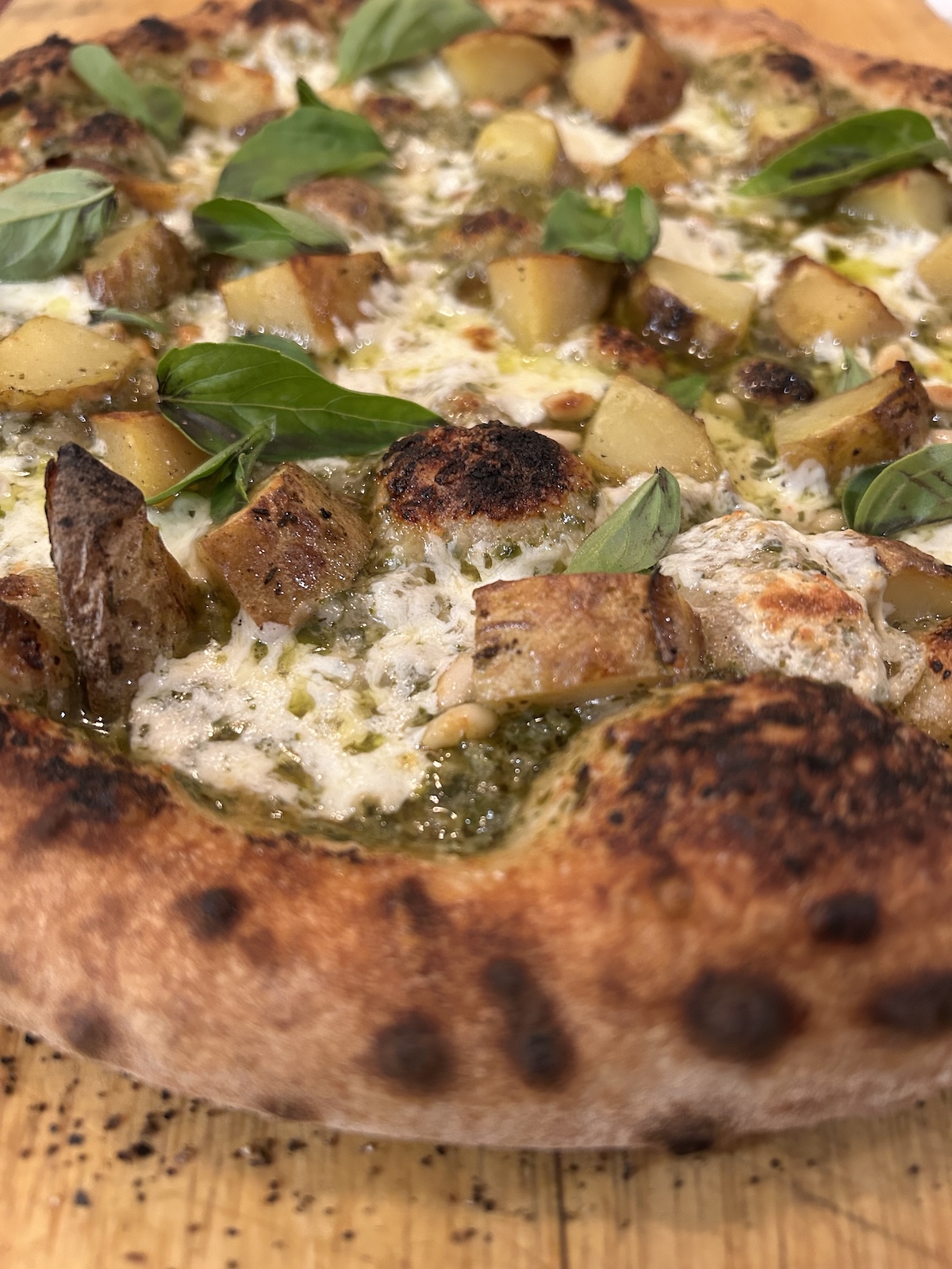 Baked pizza topped with pesto, pine nuts, potatoes, mozzarella, and fresh basil leaves.
