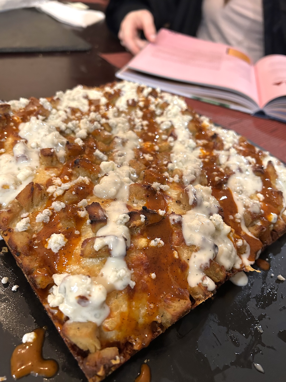 A baked square Detroit style pizza topped with Buffalo chicken, blue cheese sauce, and Buffalo hot sauce, shown from the corner.