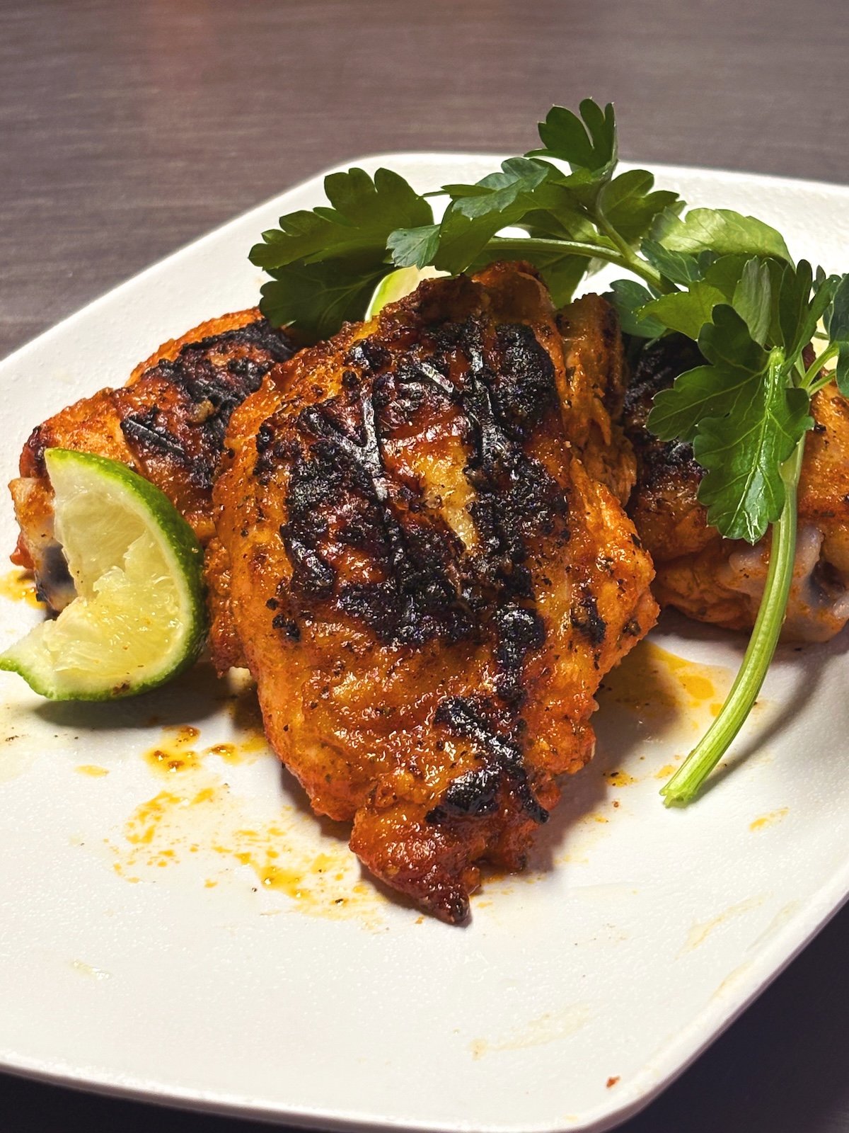 ancho lime grilled chicken thighs shown with cilantro on a white plate