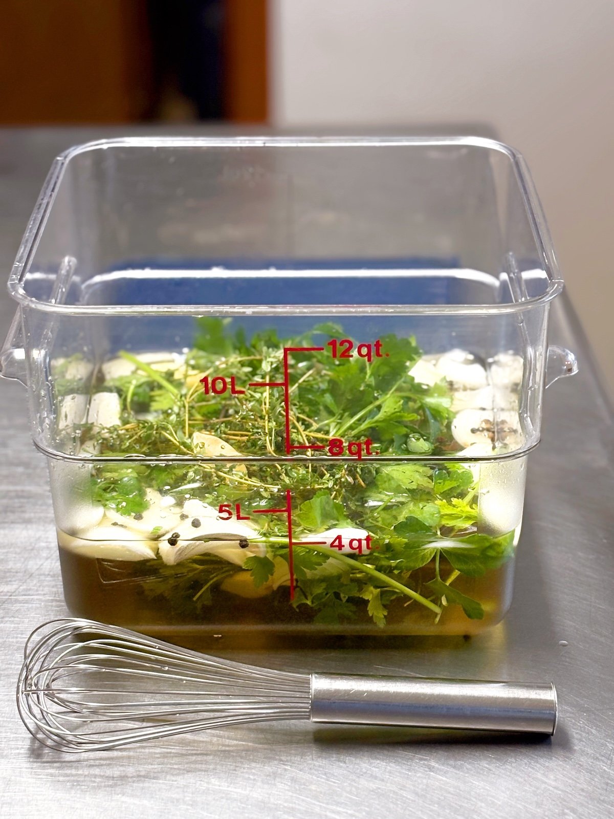 poultry brine in a clear container on a table with a whisk on the table