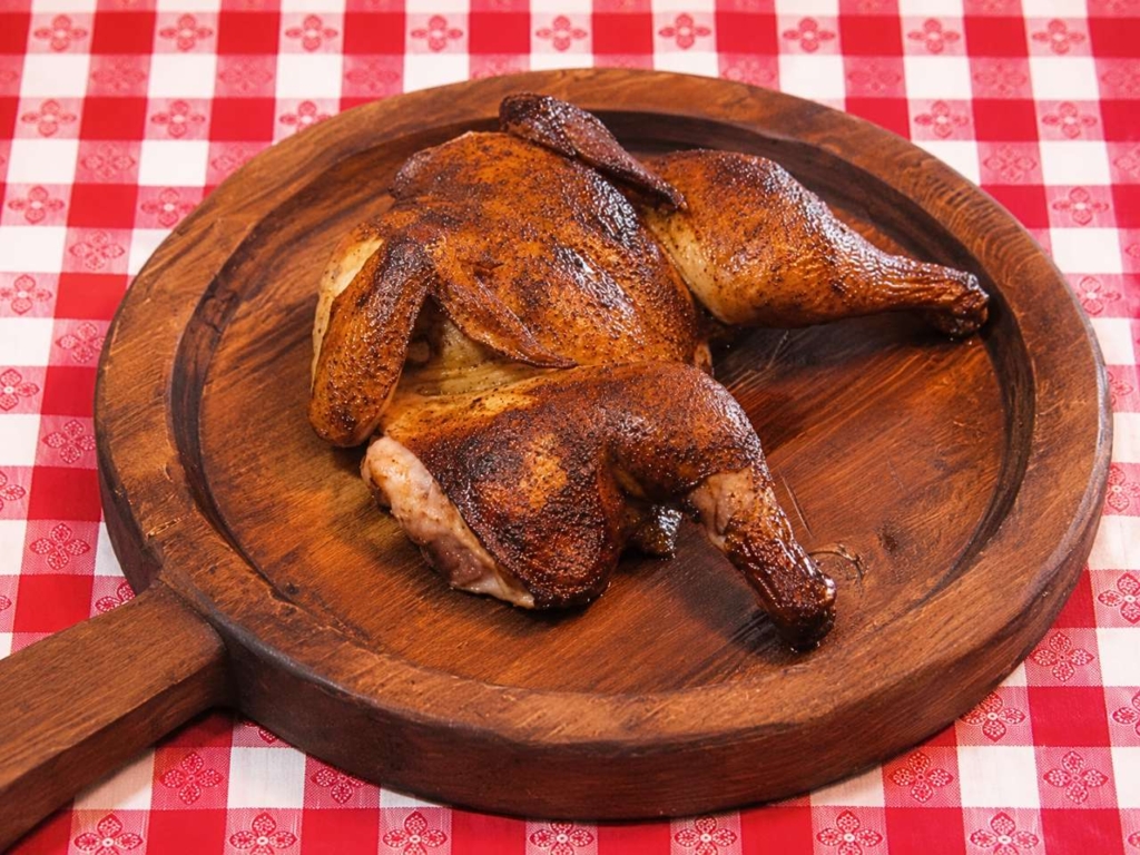 Spatchcocked chicken on a wooden board on a red checkered tablecloth.