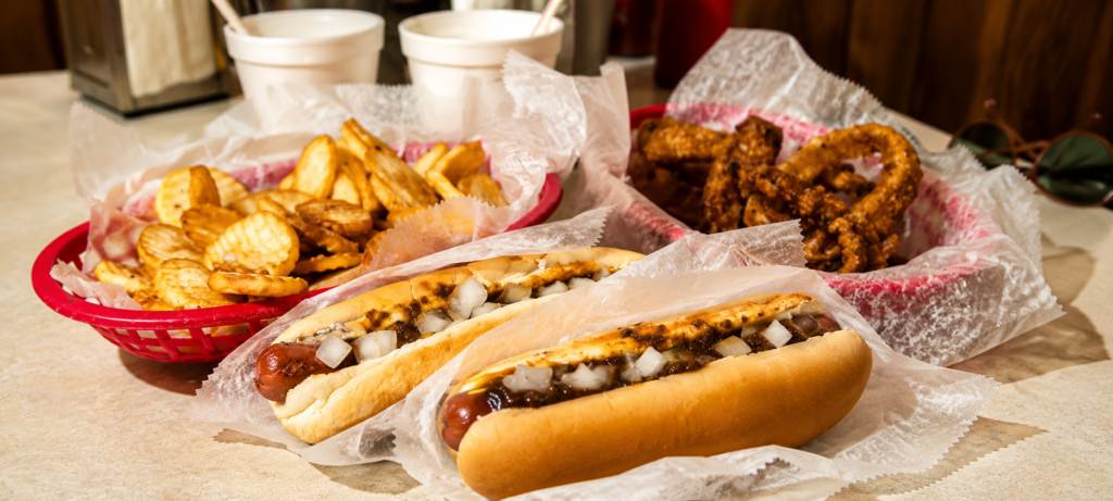 Two Detroit Coney hot dogs with fries and onion rings in the background