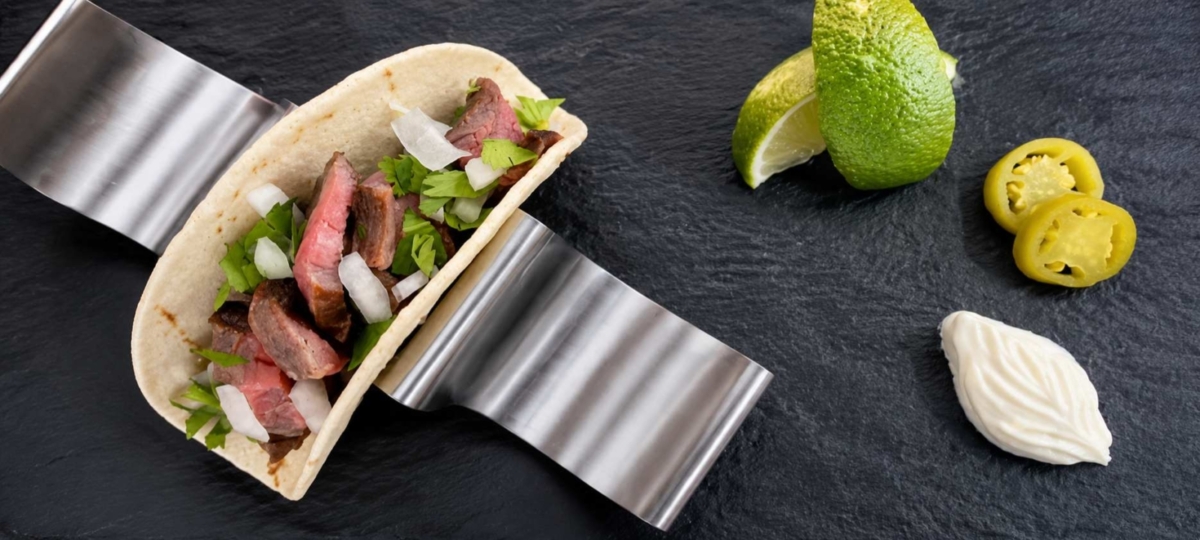 Flank steak taco topped with onion and cilantro on a plate next to limes, jalapeno slices, and sour cream