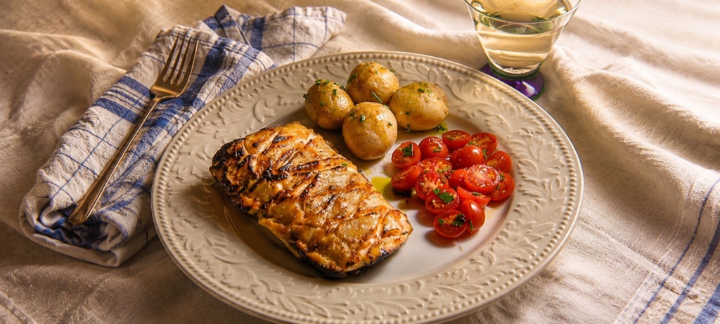 Maple salmon on a plate with potatoes and tomatoes.