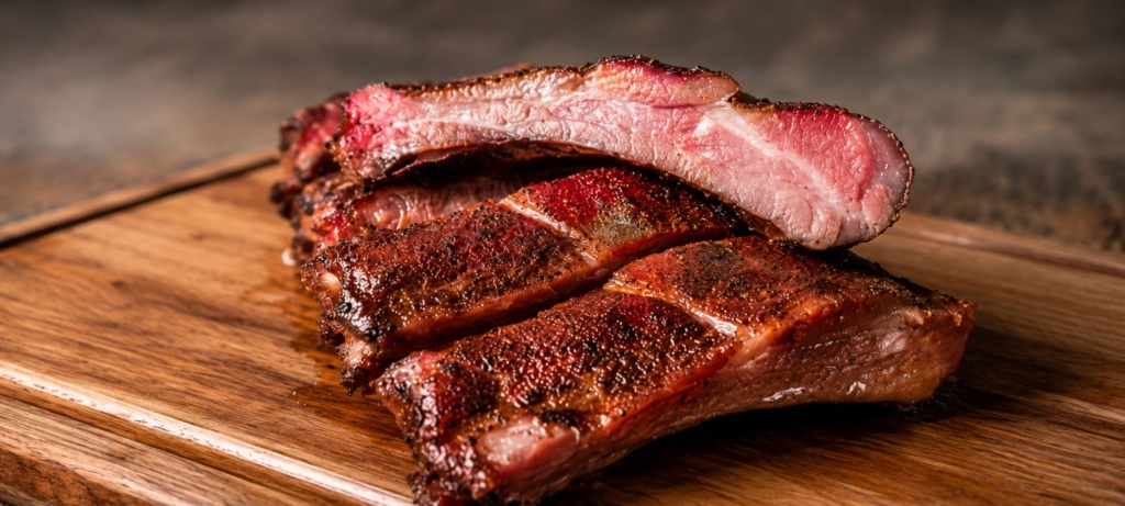 Smoked bacon ribs sliced and stacked on a wooden cutting board.