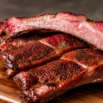 Smoked bacon ribs sliced and stacked on a wooden cutting board.