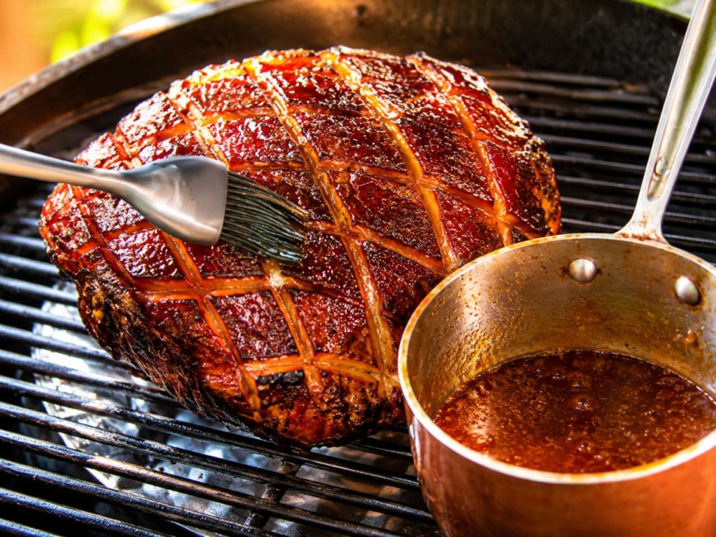Double smoked ham on a grill bring brushed with glaze.