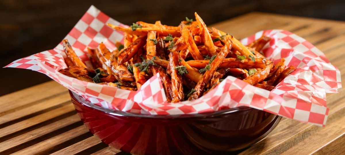 Sweet potato fries with spicy honey and fried sage leaves in a red bowl with checkered paper