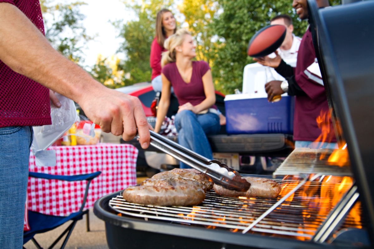 tailgating with a grill in the foreground and people laughing in the background.