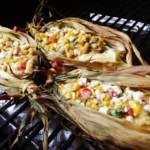 elote dip shown in the corn husks on a grill