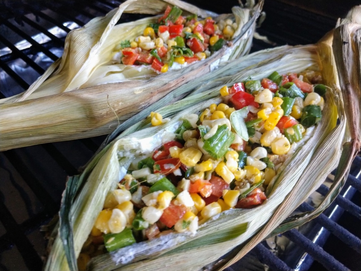 elote dip shown in the corn husks on a grill